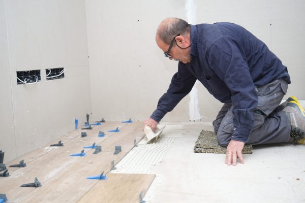 Tiler putting tiles adhesive to the floor with the notched trowel. House renovation.